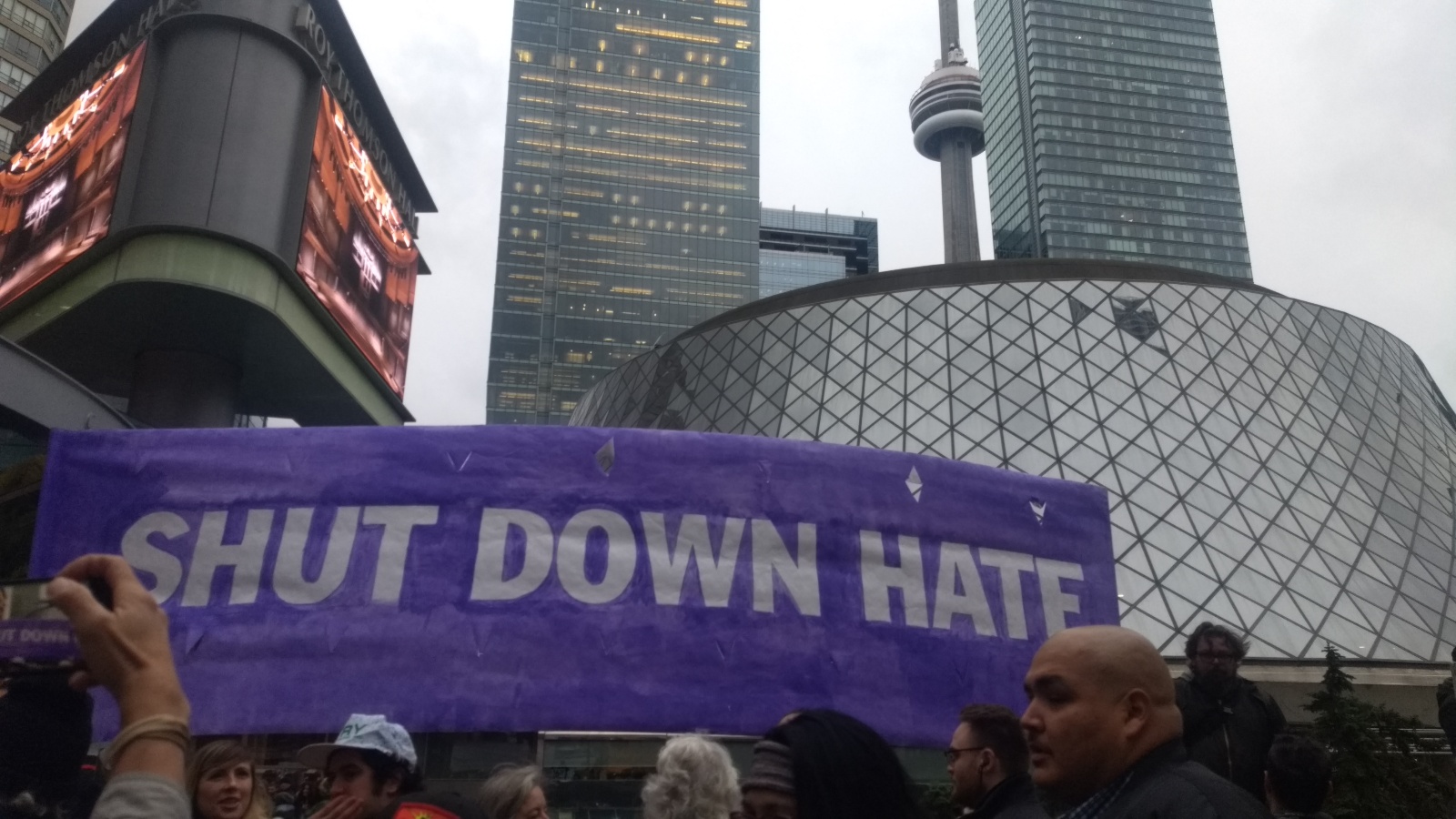Protesters hold a large banner reading "Shut Down Hate" in front of Roy Thomson Hall.