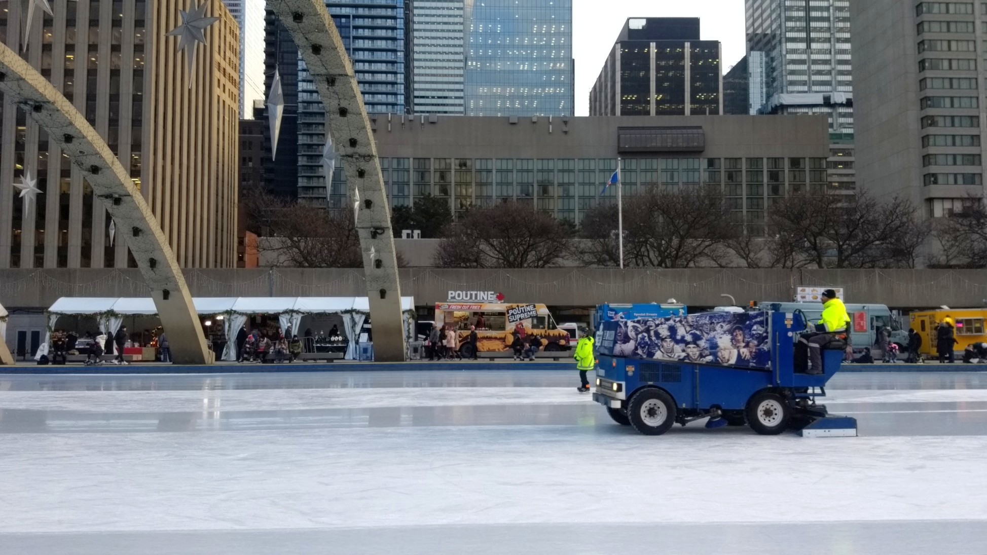 At the Nathan Phillips Square skating rink, a zamboni slowly rolls by with a poutine truck in the background.