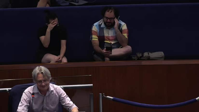 Me (in black, left) and Goldsbie (in colourful shirt, right) both facepalm with embarrassment in the Council Chamber gallery while Perks is in the foreground, beaming.