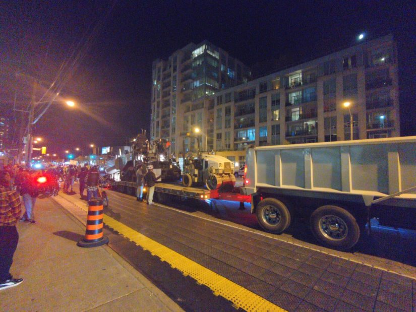 Protesters crowd around a dump truck with a trailer loaded with more equipment to prevent it unloading.