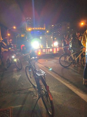 A small group of cyclists standing in front of another tractor-trailer to prevent it from moving.