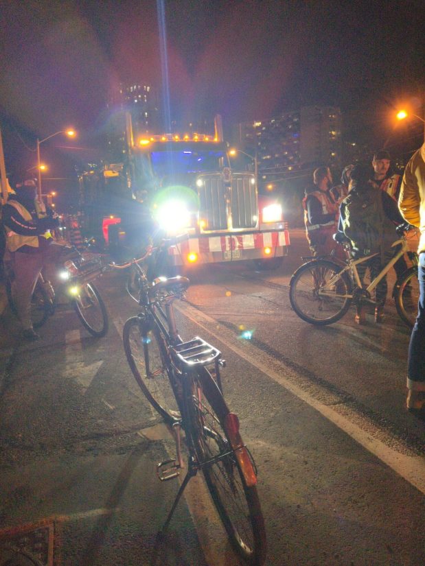 A small group of cyclists standing in front of another tractor-trailer to prevent it from moving.
