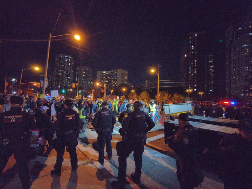 A large group of protesters behind one of the trucks are surrounded by police.