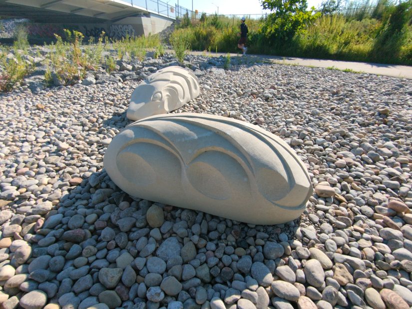 Two stone sculptures on a cobble beach; they seem like frogs?